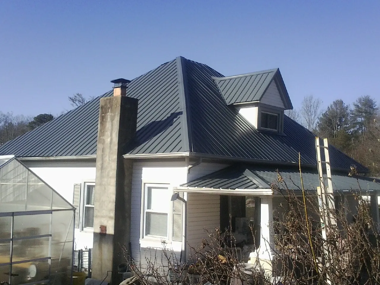 Dark blue standing seam metal roof on a white farmhouse with dormer — Slate & Tile Roof Repair by Roofing Brothers in Tillman