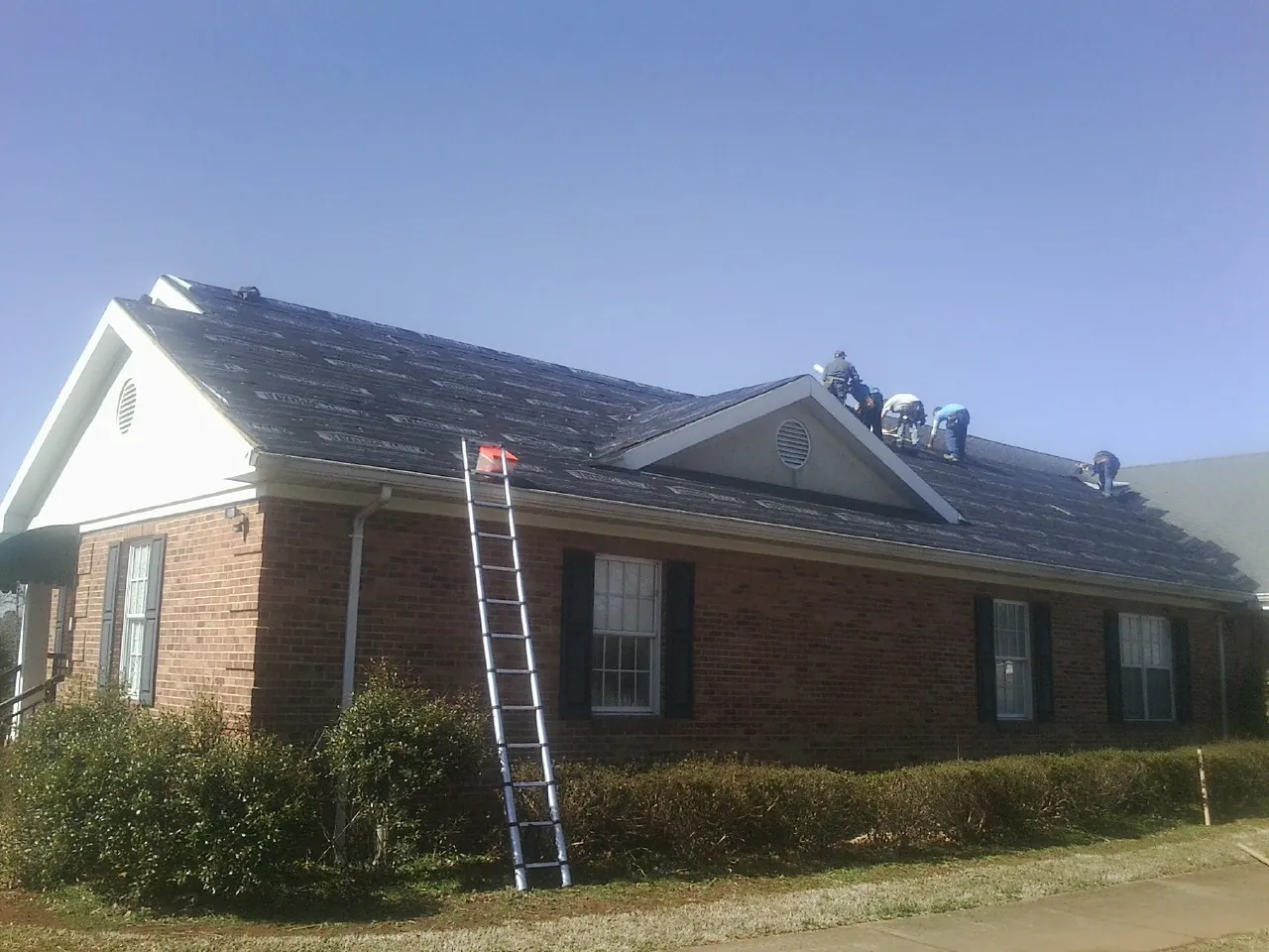 Crew tearing shingles off a brick ranch roof with a ladder set — Metal Roof Repair work by our crew in Tillman