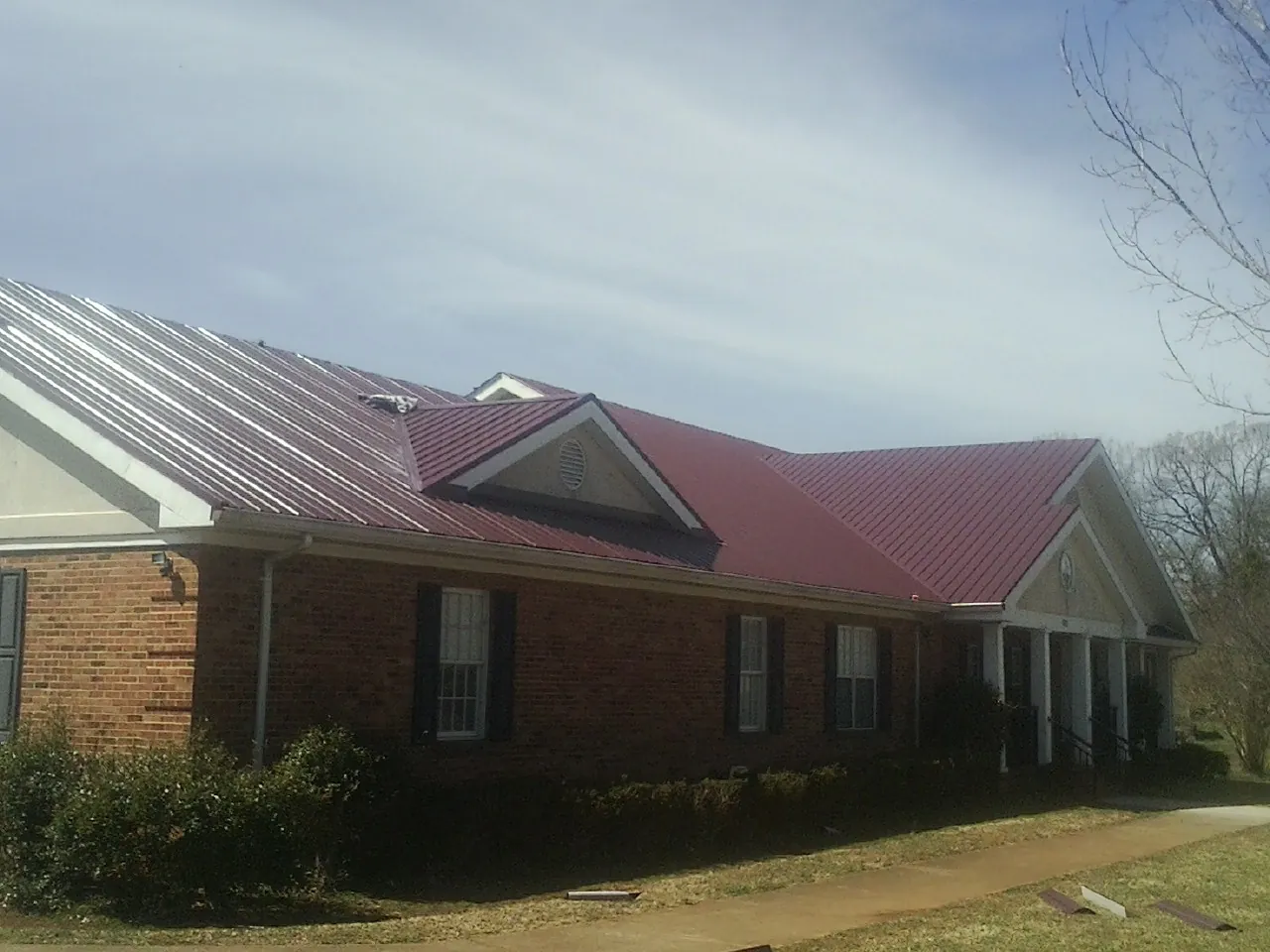 Red metal roof with gabled entries on a long brick building, from a Hail Damage Roof Repair job in Tillman