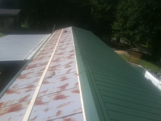 Old rusted panels beside newly installed green metal roofing — Wind Damage Roof Repair by Roofing Brothers in Tillman