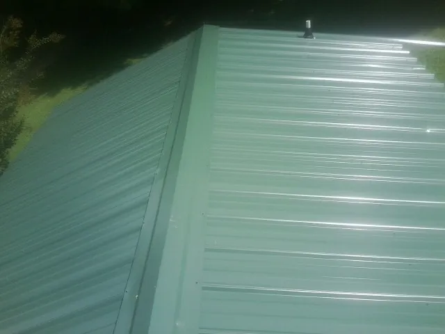 New green metal panels meeting at the ridge of a roof — Flat Roof Repair work by our crew in Tillman