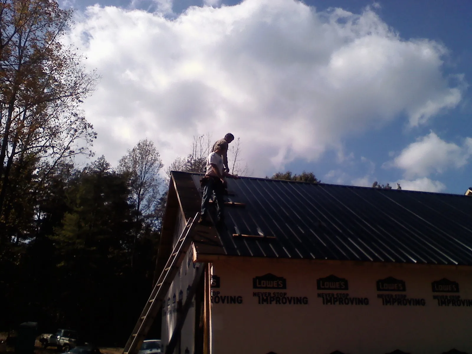Roofer fastening dark metal panels high against a cloudy sky, from a Roof Inspection job in Tillman