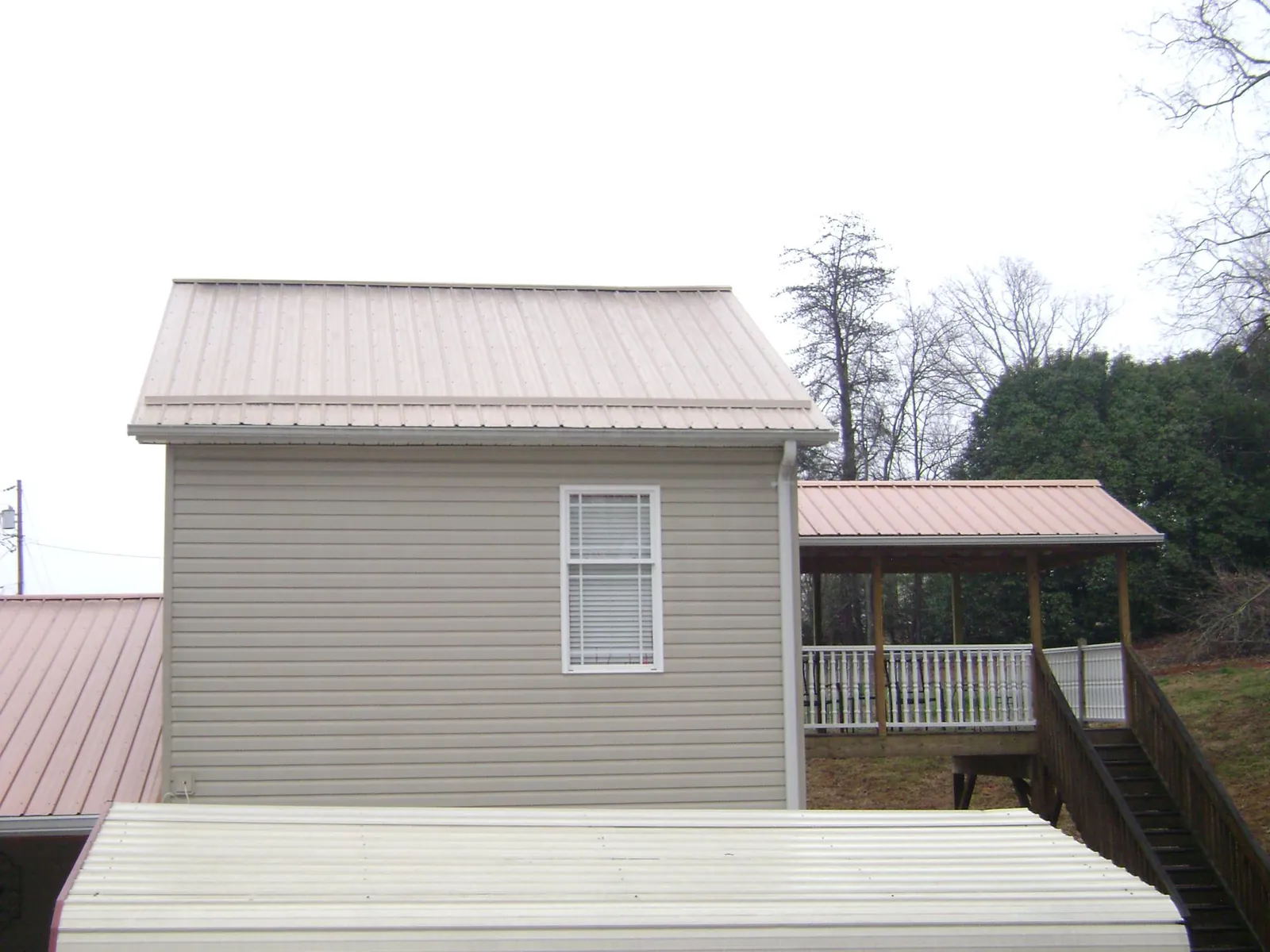 Tan metal roofs on a two story addition and attached porch, from a Roof Replacement job in Tillman